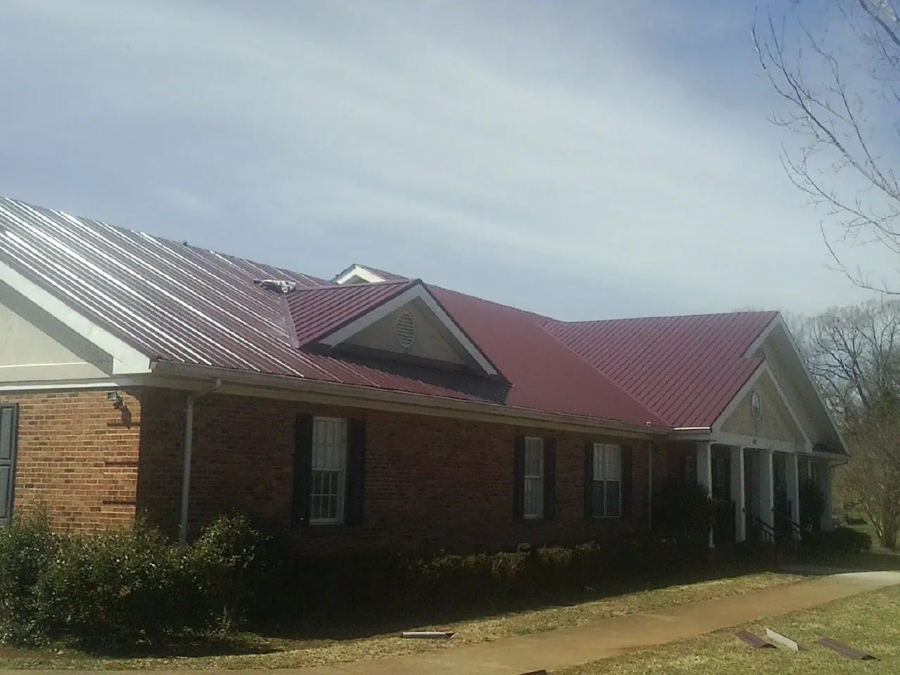 Red metal roof with gabled entries on a long brick building, from a Hail Damage Roof Repair job in Hubbard