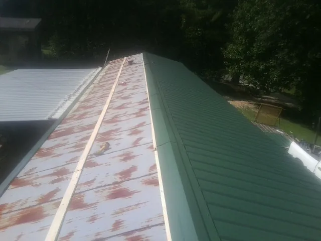 Old rusted panels beside newly installed green metal roofing — Wind Damage Roof Repair by Roofing Brothers in Hubbard